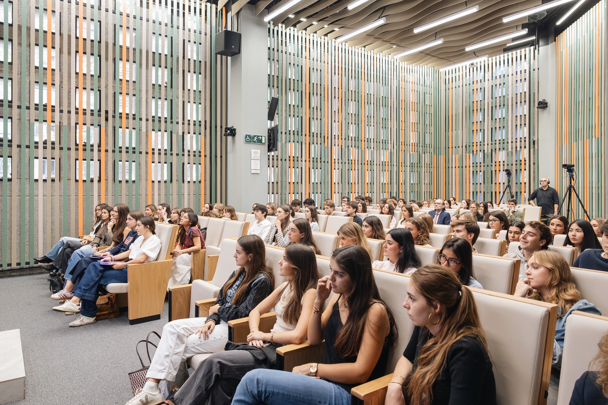 Una multitud de jóvenes sentados en un auditorio moderno escuchando atentamente.