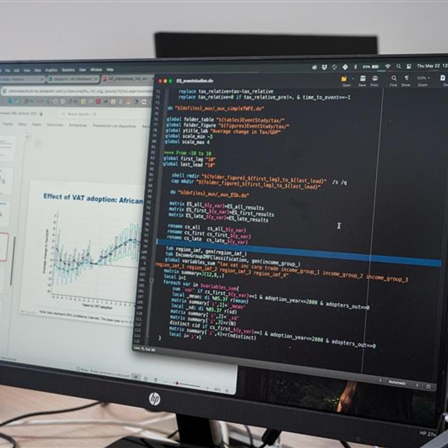 La imagen muestra un monitor con un código de programación abierto y gráficos de datos en una ventana diferente.