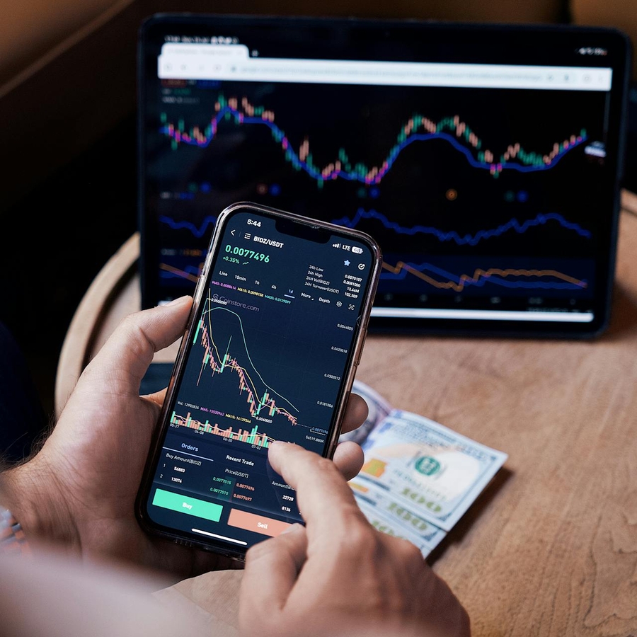 Una persona analiza gráficos financieros en su teléfono móvil frente a una tablet con datos de mercado.