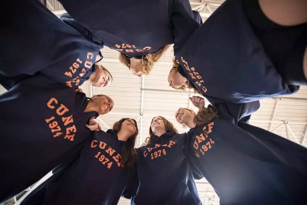 Un grupo de jóvenes se reúne en un círculo, luciendo sudaderas con el mismo diseño.