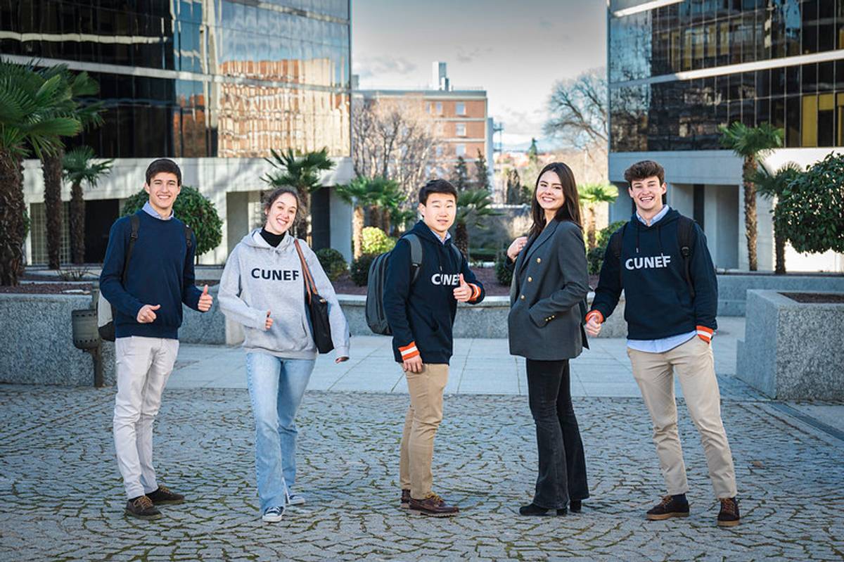 Un grupo de cinco estudiantes sonríen y posan juntos en un campus moderno.