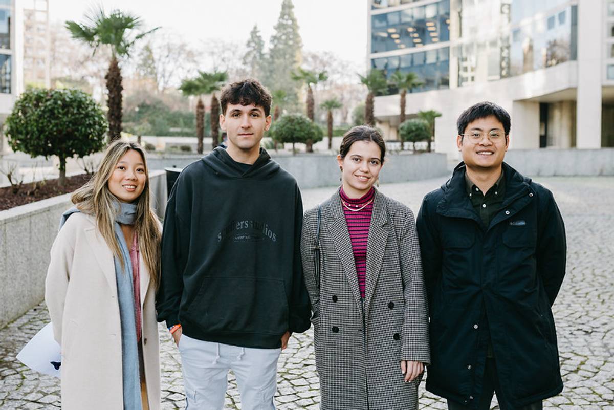 Cuatro jóvenes posan juntos al aire libre en un entorno urbano moderno.