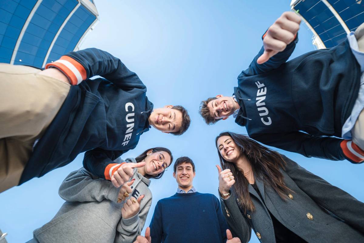 Un grupo de cinco jóvenes sonríen y hacen gestos de aprobación bajo un cielo claro.