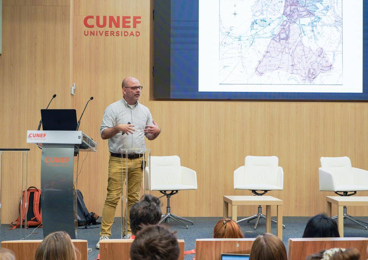 Un hombre presenta un tema en una conferencia en la universidad CUNEF, mientras una audiencia lo observa.