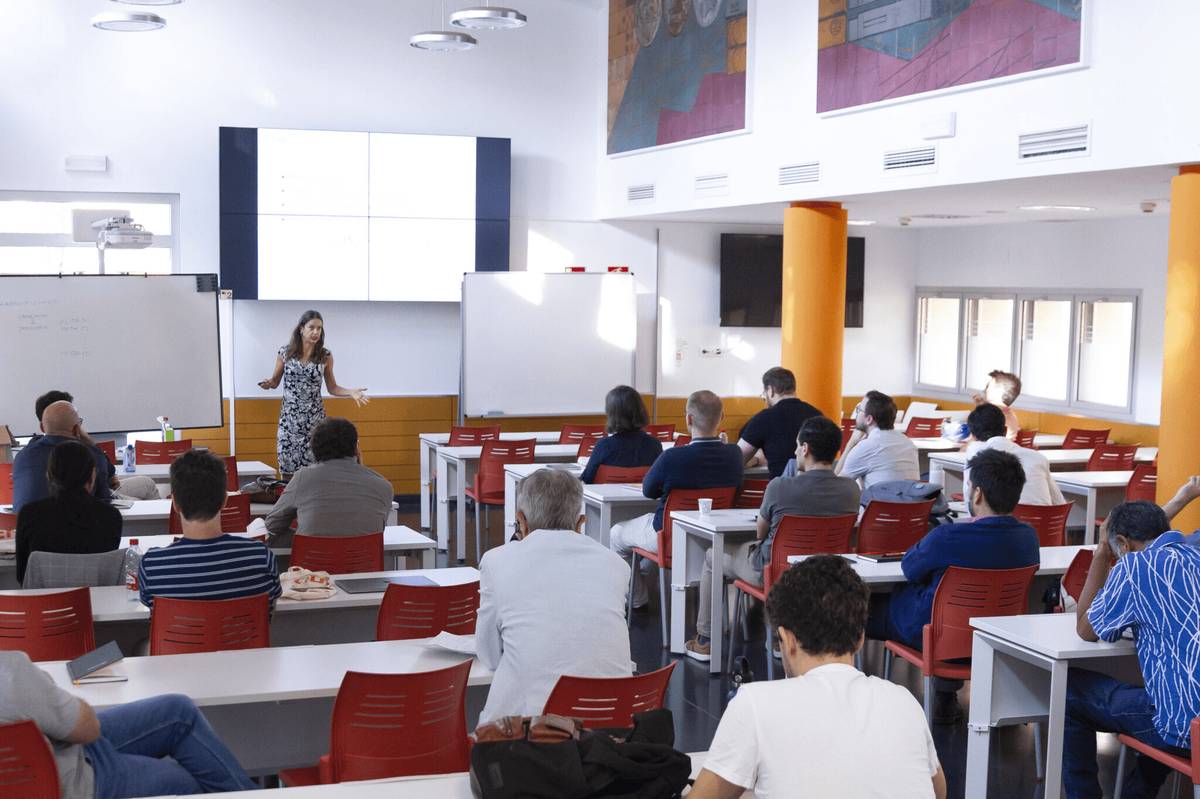 Una mujer está dando una presentación frente a un grupo de personas en un aula moderna.