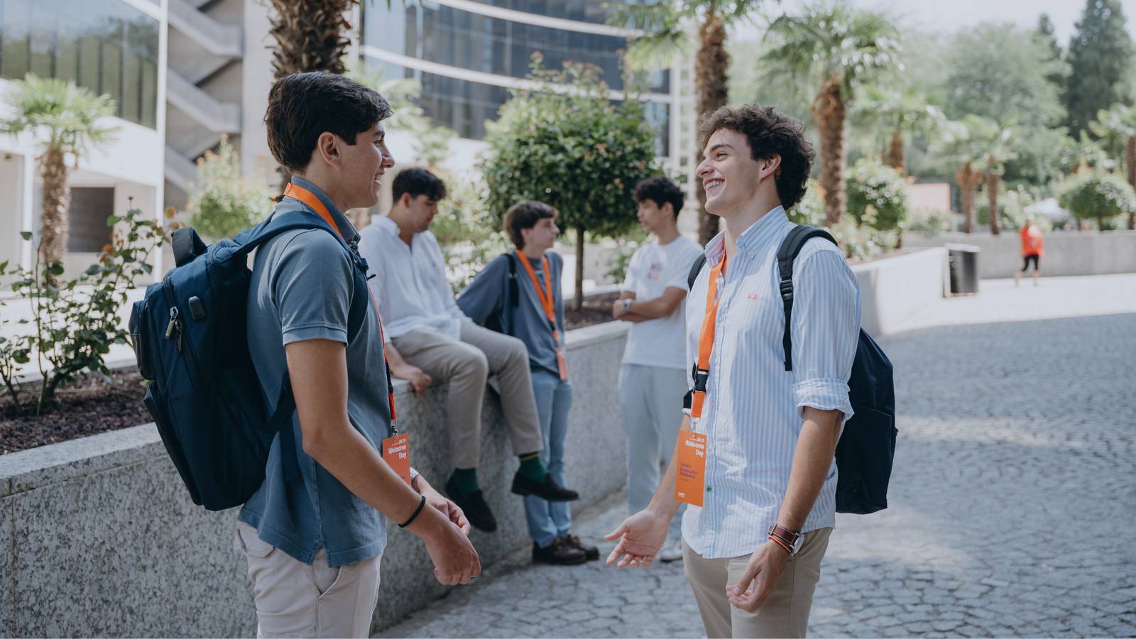 Dos jóvenes conversan animadamente en un entorno al aire libre mientras otros chicos están al fondo.