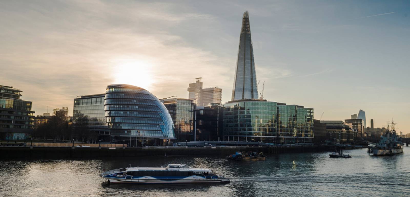 Una vista del Támesis en Londres con edificios modernos y un barco en la superficie, al atardecer.