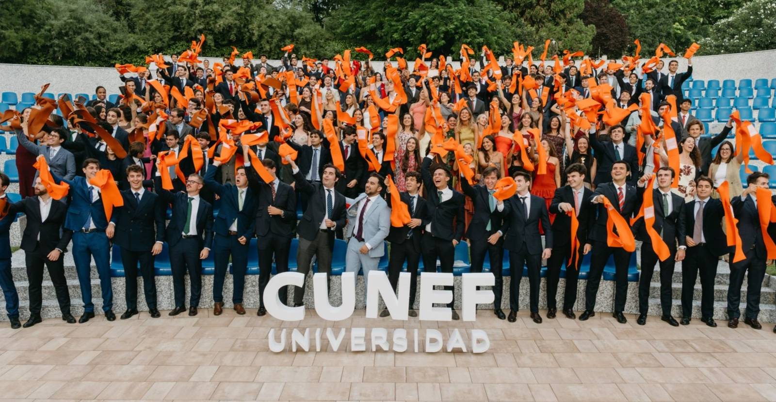 Un grupo de graduados de CUNEF Universidad celebra al aire libre con bufandas naranjas.