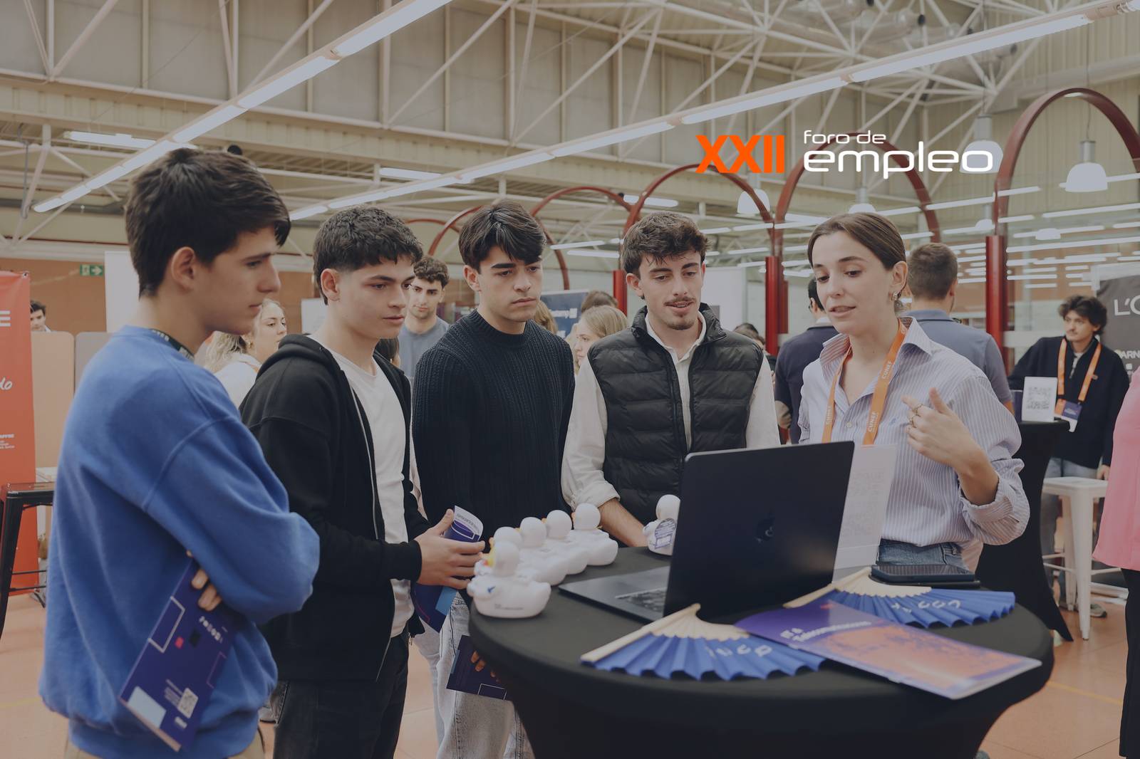 Un grupo de jóvenes observa atentamente a una mujer que está presentando información en un ordenador portátil durante un foro de empleo.