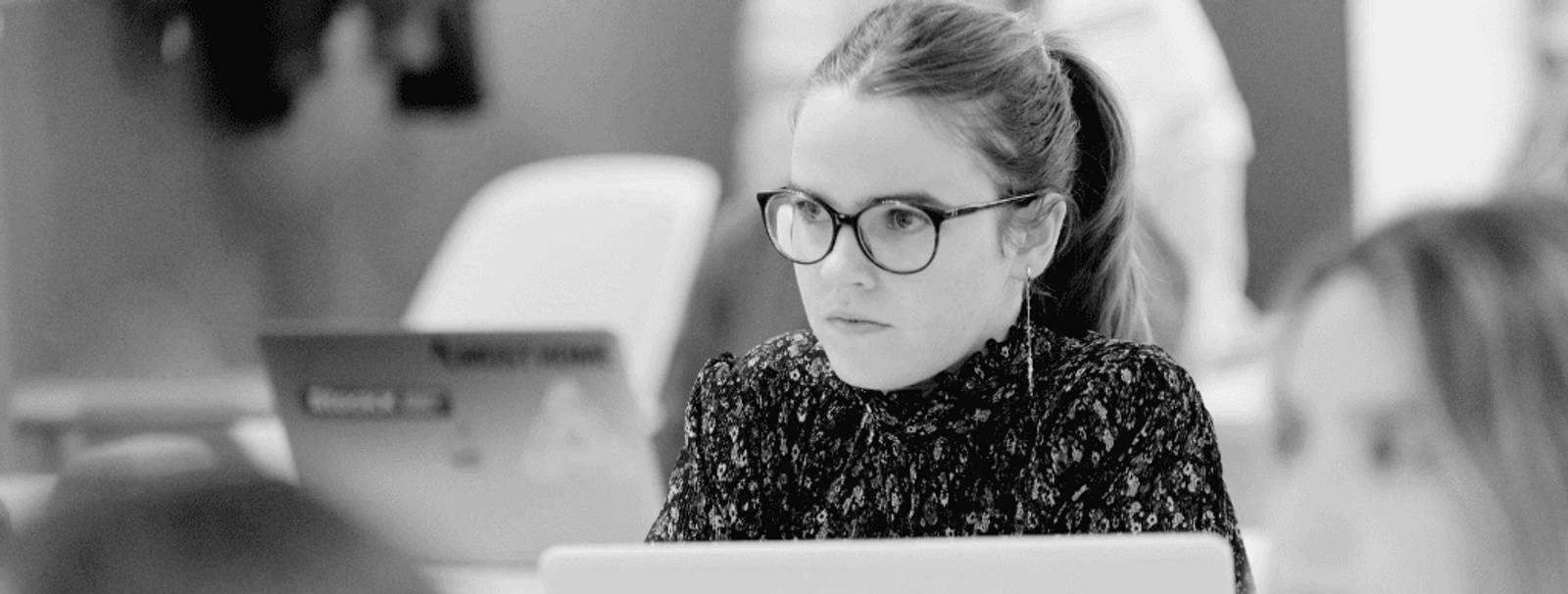 Una mujer con gafas observa atentamente frente a una computadora portátil en un entorno de trabajo.