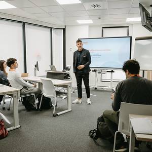 Un grupo de personas escucha a un presentador en una sala de clases moderna.