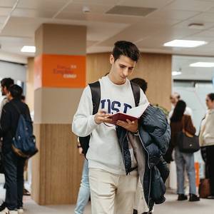 Un estudiante revisa un libro mientras camina por un espacio académico.