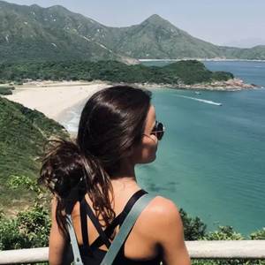Una mujer observa un paisaje de montaña y mar desde un mirador.