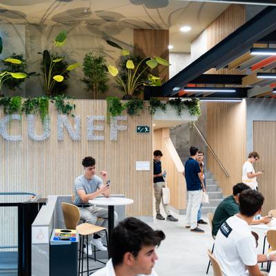 Una vista del interior de un espacio moderno de estudio con plantas decorativas y estudiantes trabajando en mesas.