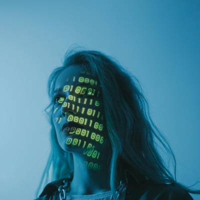 Una mujer con un fondo azul y números en código binario proyectados en su rostro.