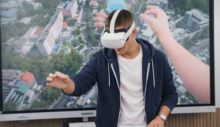 Un joven usa un visor de realidad virtual mientras interactúa con una pantalla que muestra una escena aérea de una ciudad.