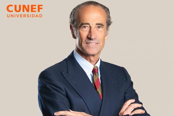 Un hombre de negocios con vestimenta formal y una sonrisa, posando frente a un fondo neutral.