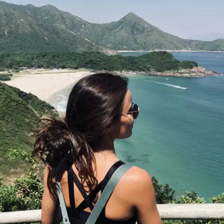Una mujer observa un paisaje de montaña y mar desde un mirador.