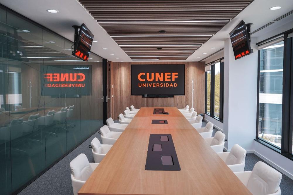 Sala de reuniones moderna de la universidad CUNEF con una larga mesa y pantallas electrónicas.