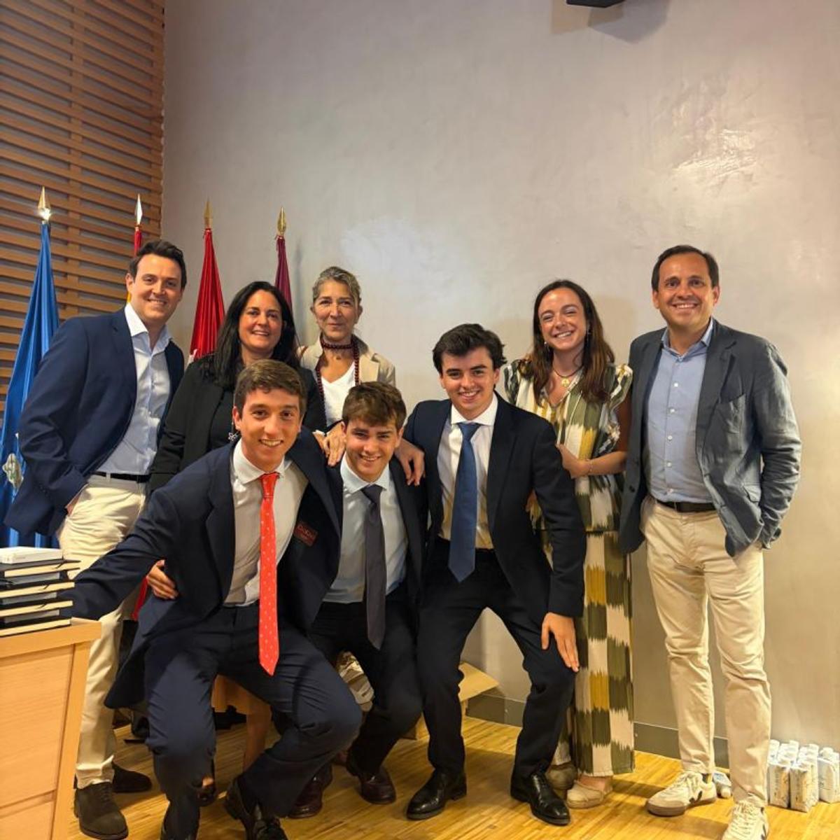 Un grupo de siete personas sonríe juntas en una habitación con banderas al fondo.