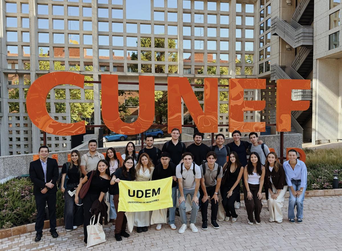 Un grupo de estudiantes posando frente al letrero de la universidad CUNEF con una bandera de UDEM.