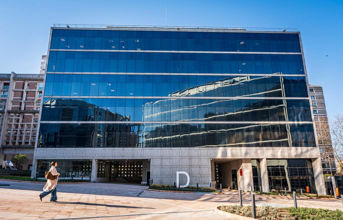Edificio moderno con fachada de vidrio y un reflejo en su superficie, en un día soleado.
