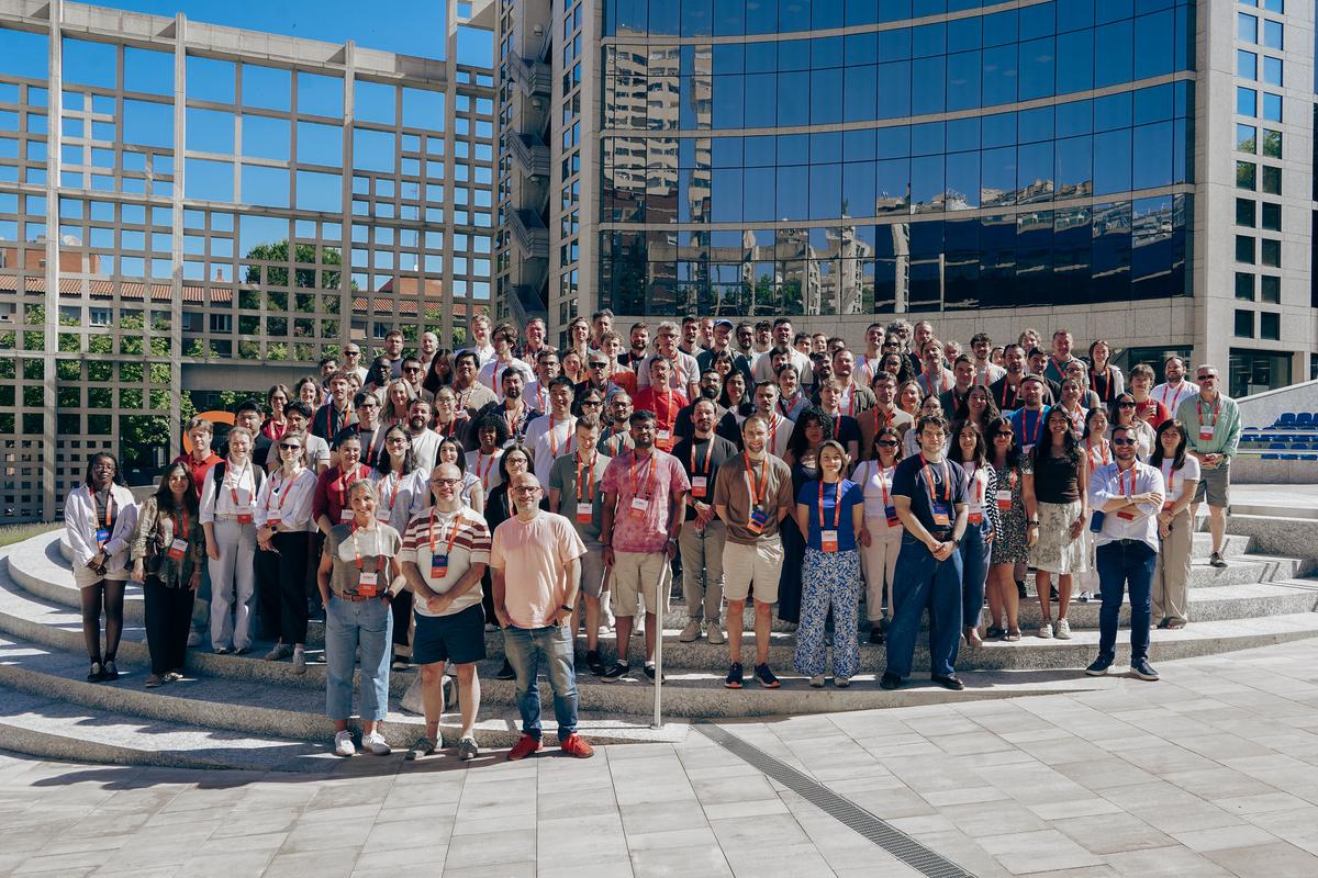 Un gran grupo de personas posando juntas en un lugar al aire libre frente a edificios modernos.