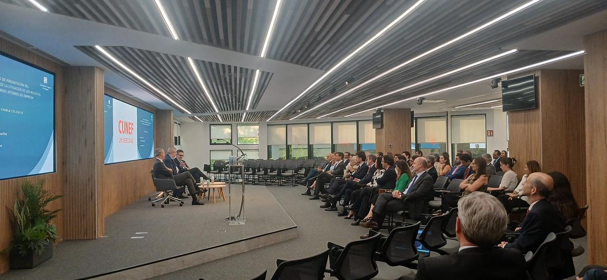 Una sala de conferencias con un público atento mientras dos oradores presentan en un evento formal.