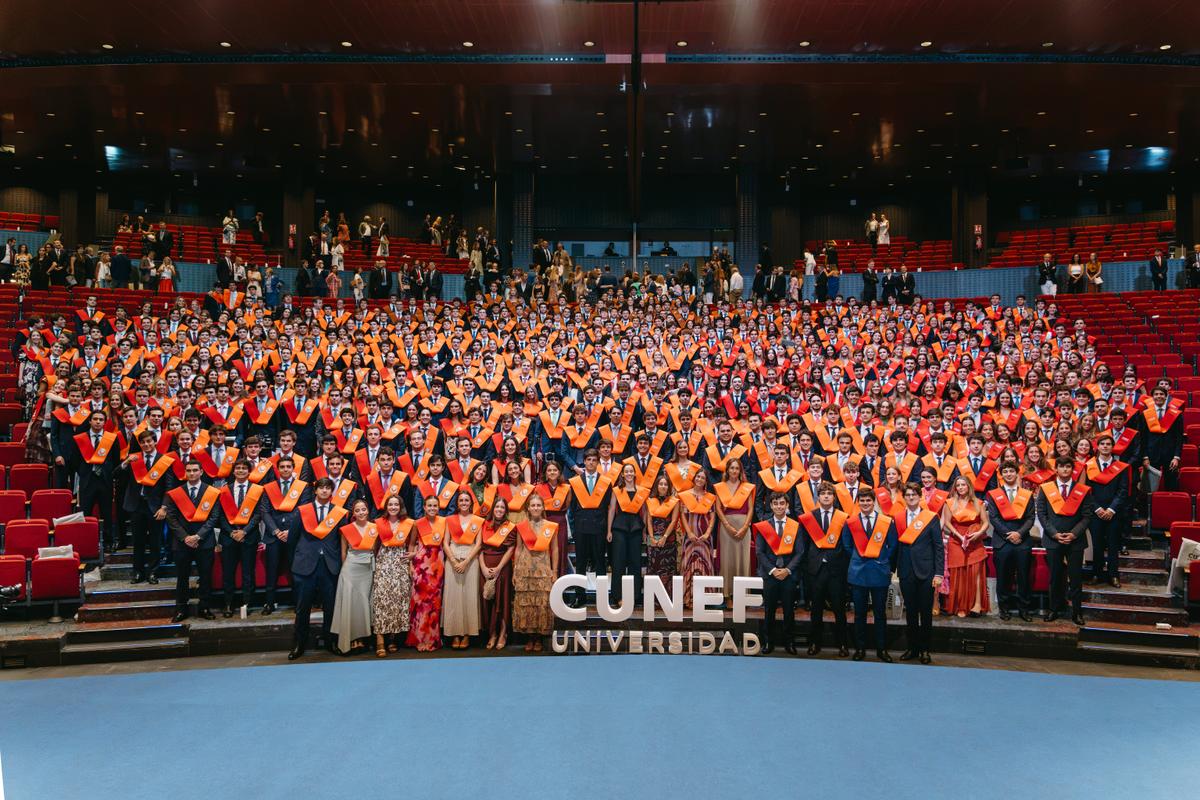 Una multitud de graduados en ceremonia académica con togas y birretes en un auditorio.