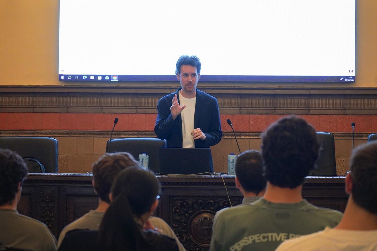 Un hombre da una presentación frente a una audiencia sentada en un aula.