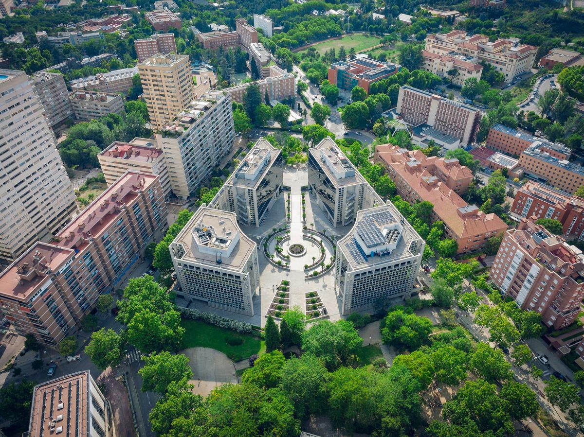 Vista aérea de un complejo arquitectónico rodeado de áreas verdes y edificios en una ciudad.