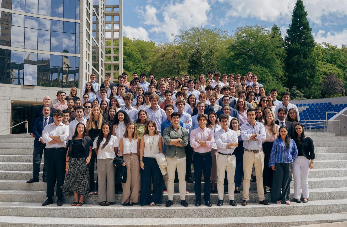 Un grupo grande de personas posando en una escalinata al aire libre, con un edificio moderno y árboles al fondo.