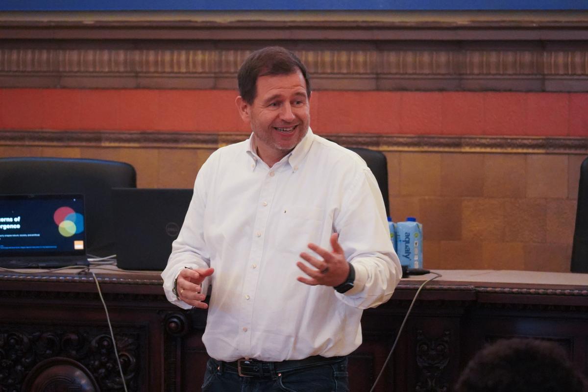 Un hombre sonriente se encuentra de pie mientras habla en un evento, gesticulando con las manos.