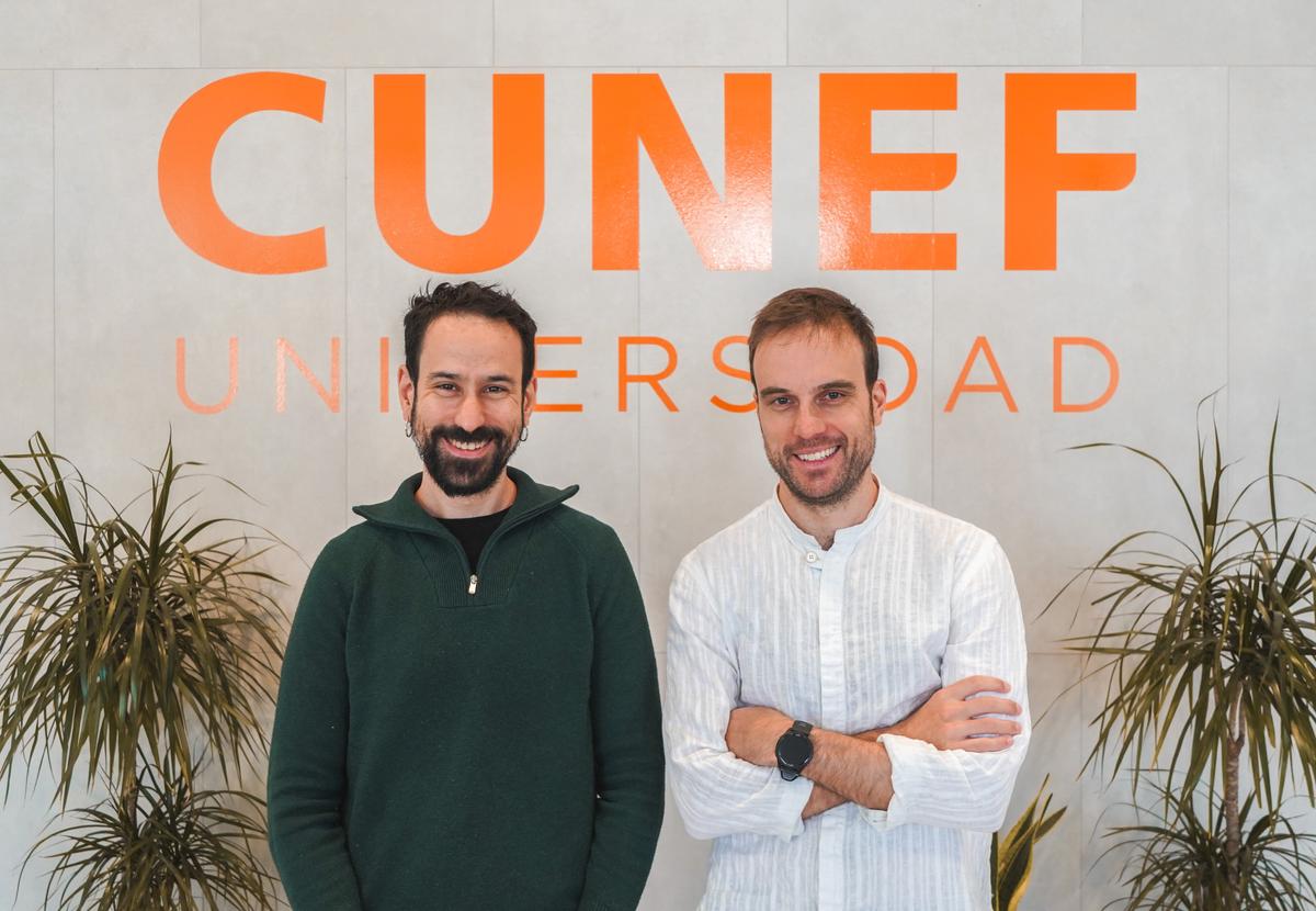 Dos hombres sonrientes posan frente a un fondo con el nombre de una universidad.
