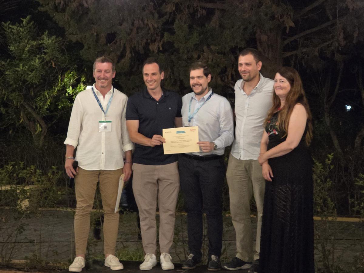 Un grupo de cinco personas sonríe mientras sostienen un certificado en un entorno al aire libre.