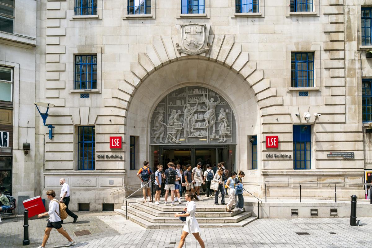 La imagen muestra la entrada del edificio Old Building de la London School of Economics, con un grupo de estudiantes en la entrada.