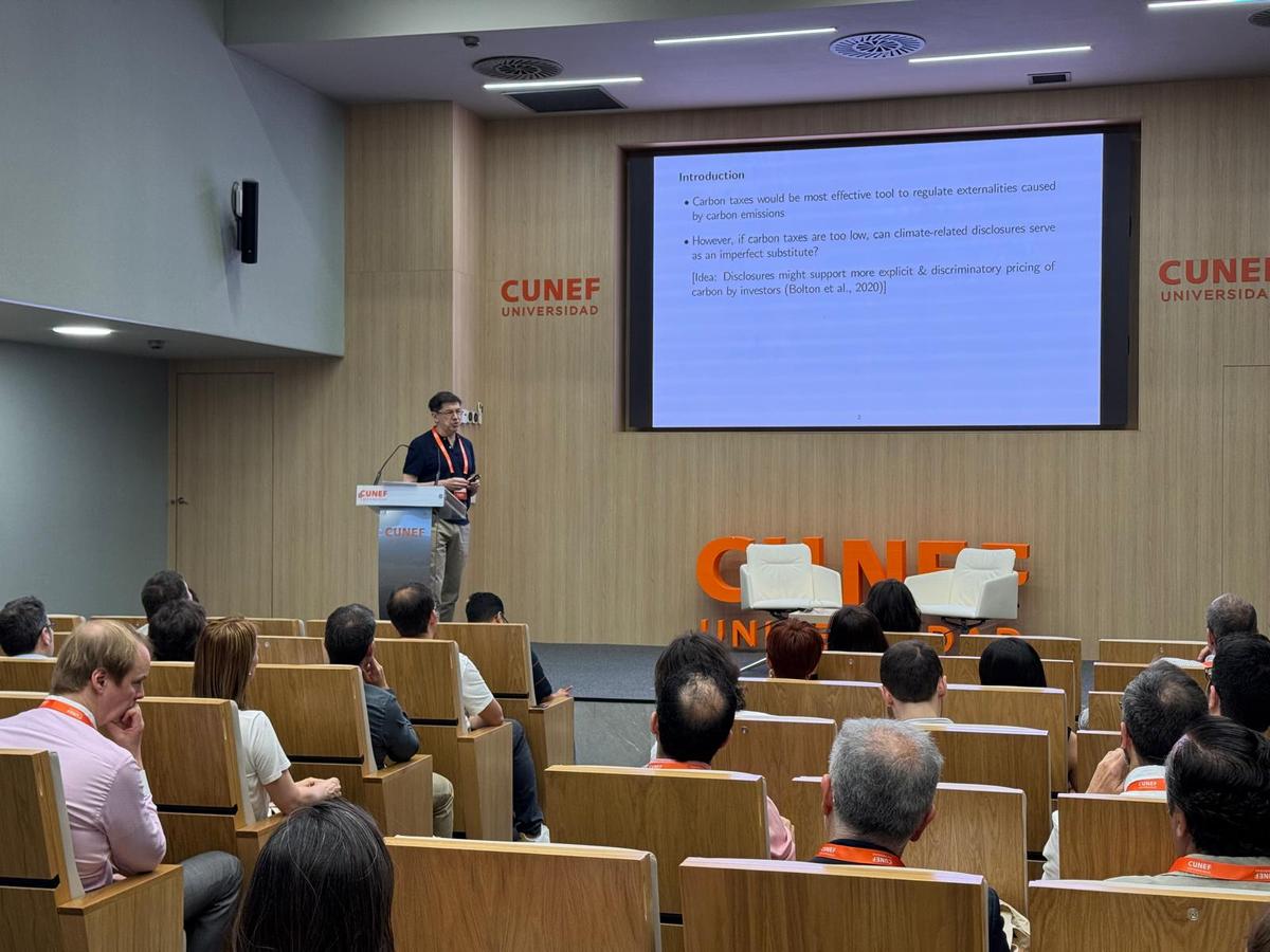Un ponente presenta en una conferencia ante un público sentado en un auditorio.