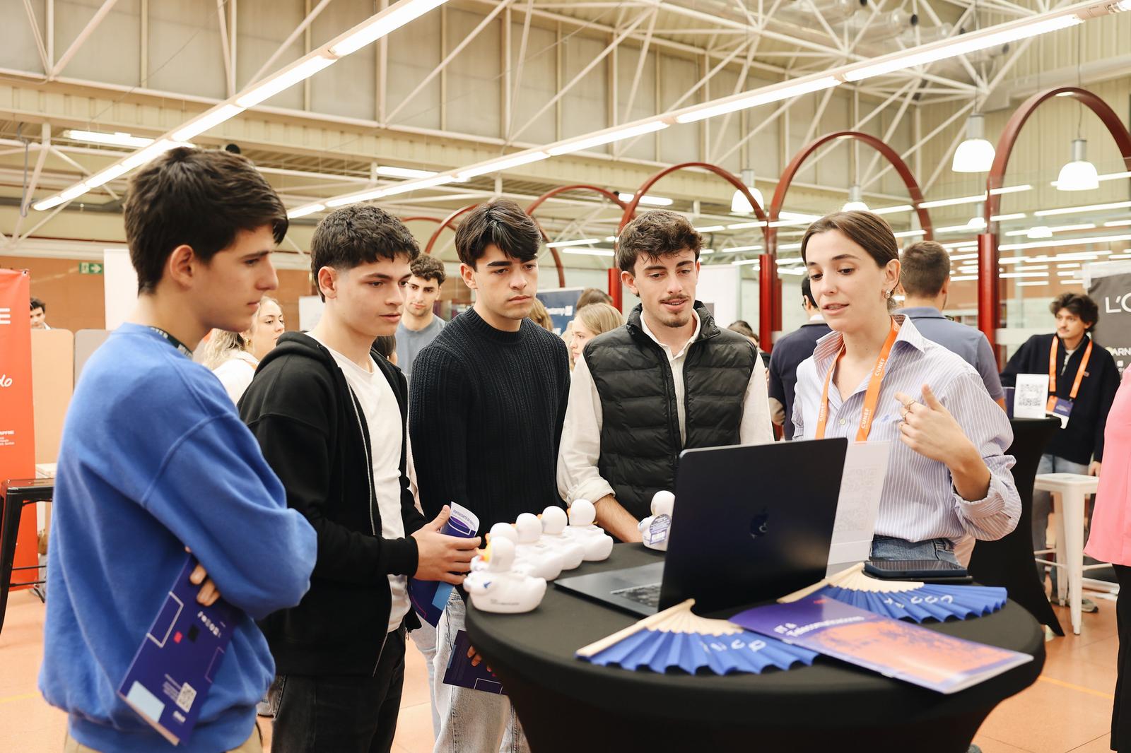Un grupo de jóvenes escucha atentamente a una mujer que presenta información en una laptop durante un evento.