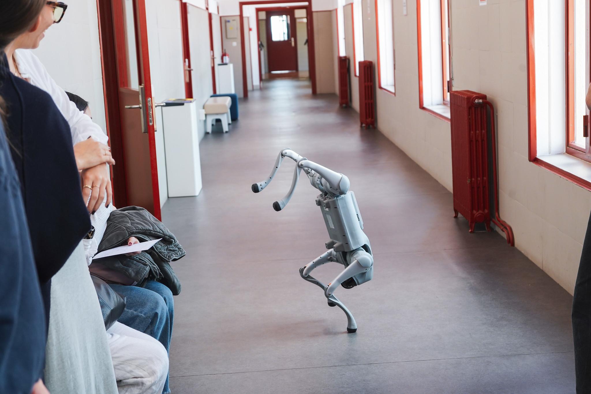 Un robot con forma humanoide se encuentra de pie en un pasillo mientras varias personas lo observan.