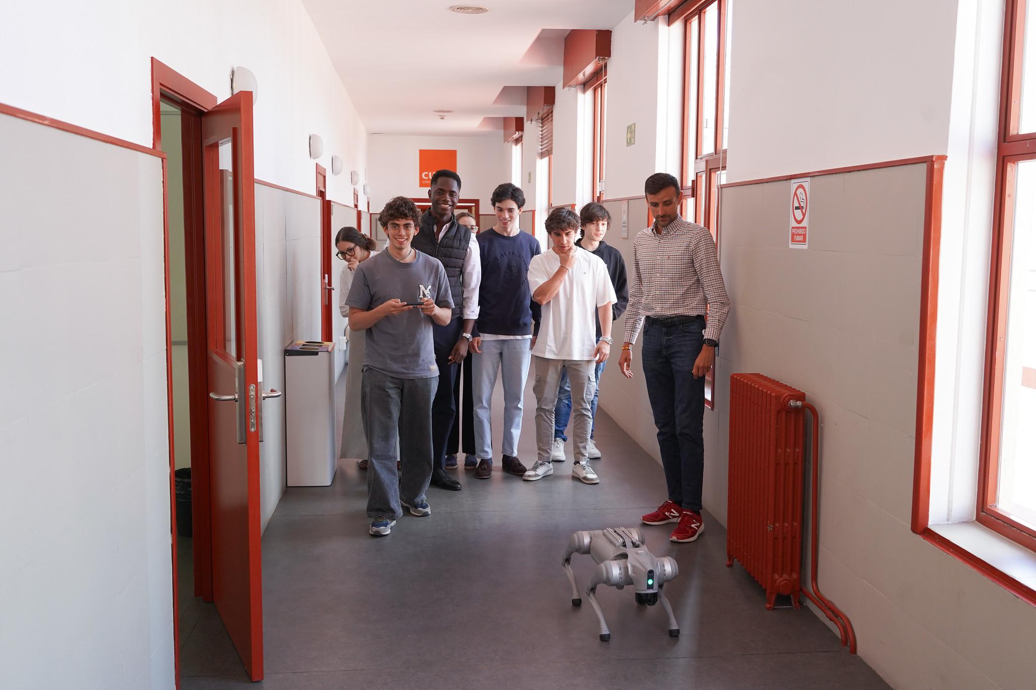 Un grupo de estudiantes observa un robot caminando por un pasillo escolar.