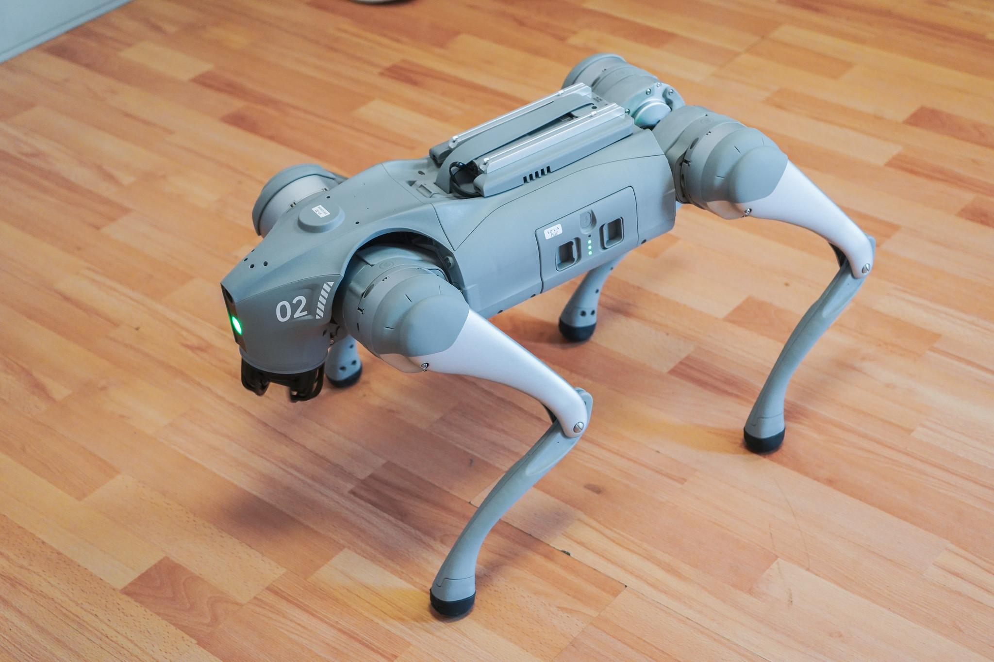 Un robot cuadrúpedo gris sobre un suelo de madera.
