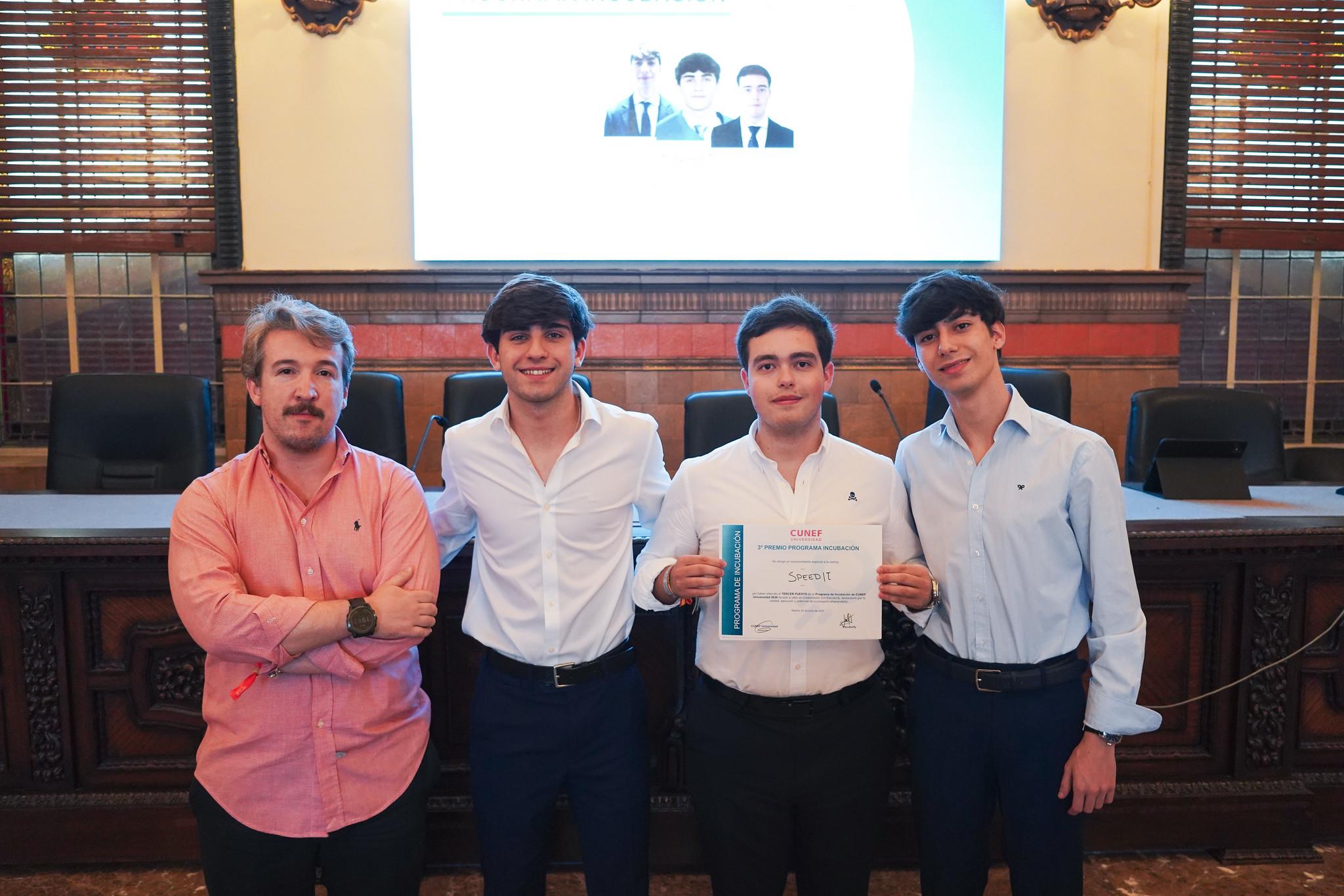 Cuatro jóvenes posando con un certificado en un evento formal.