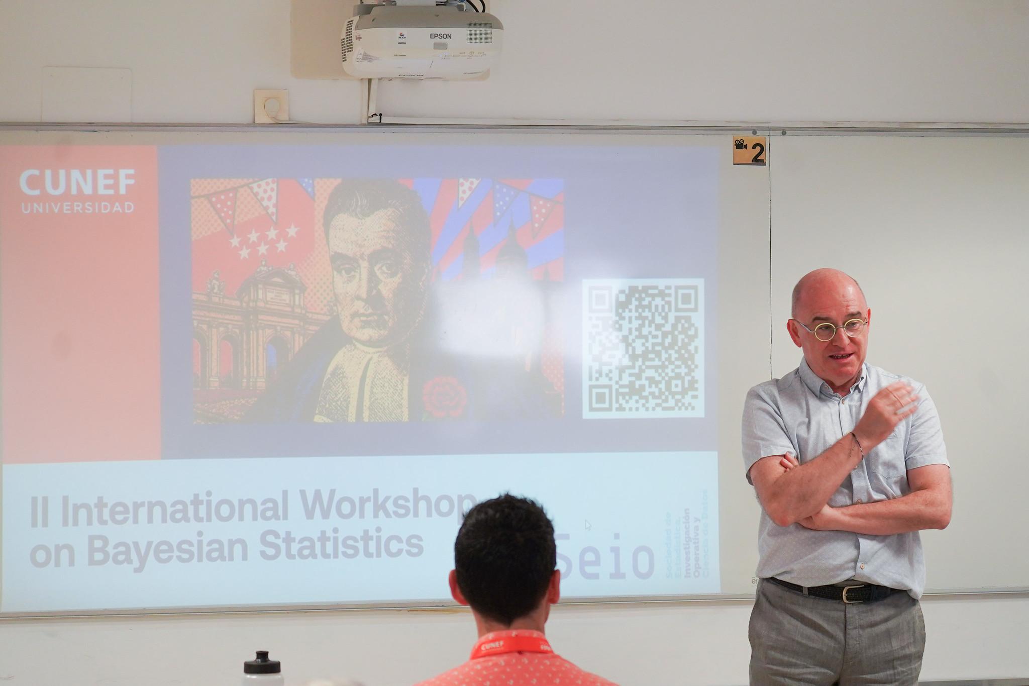 Una persona está dando una charla en un taller internacional sobre estadísticas bayesianas en una sala con una proyección visible detrás.