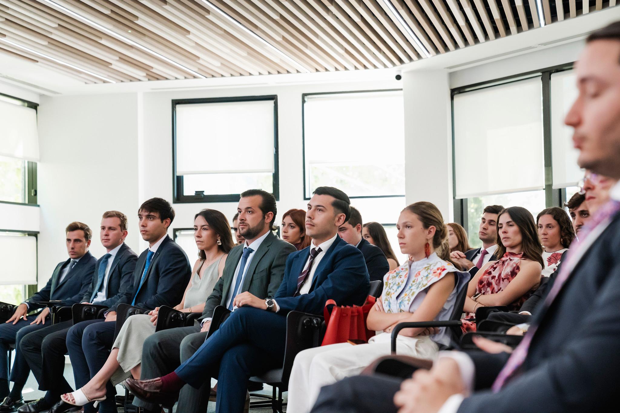 Un grupo de personas vestidas de manera formal está sentada en un salón contemporáneo.