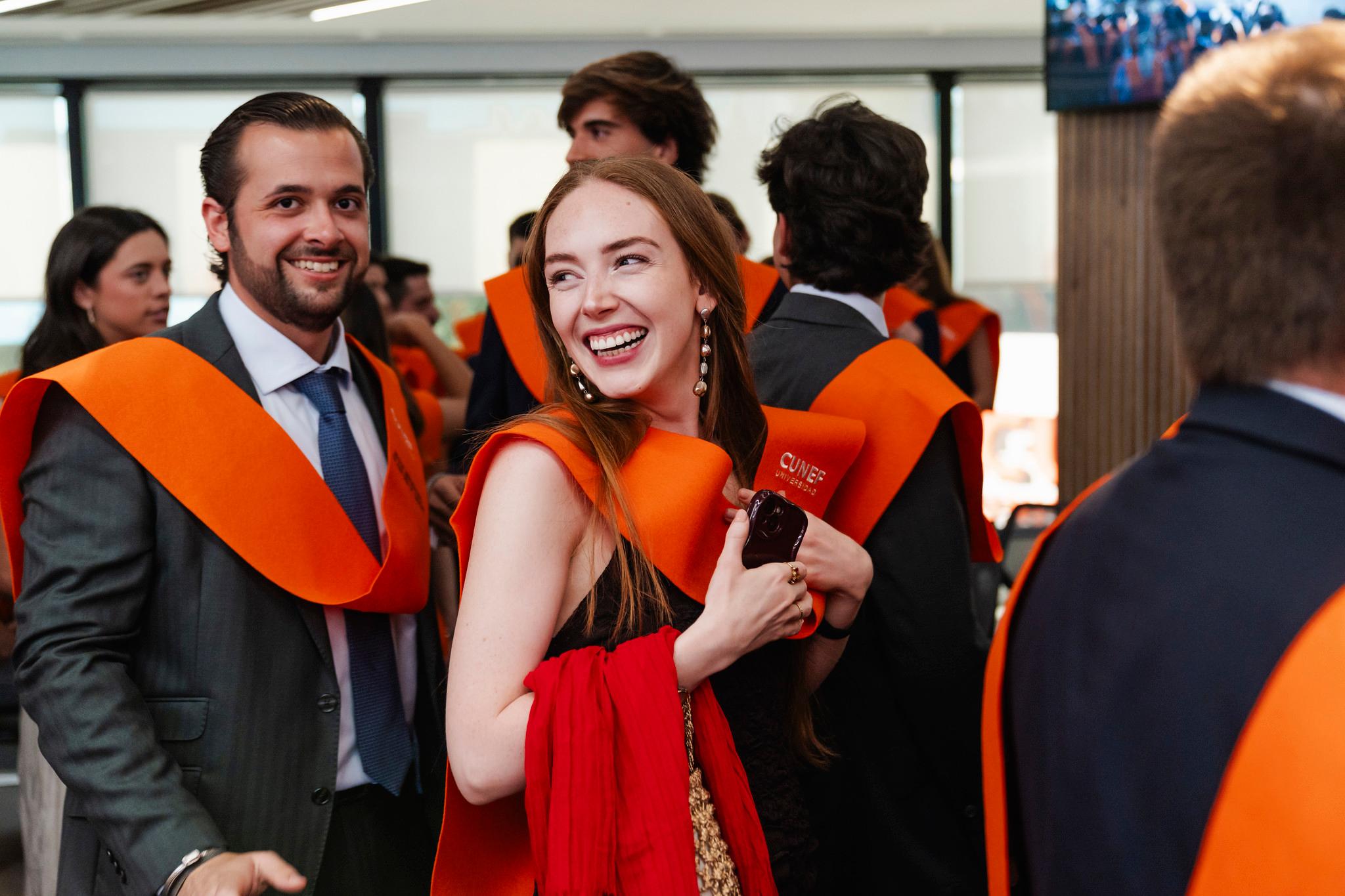 Un grupo de graduados sonríen y celebran con togas y cintas naranjas en un evento festivo.