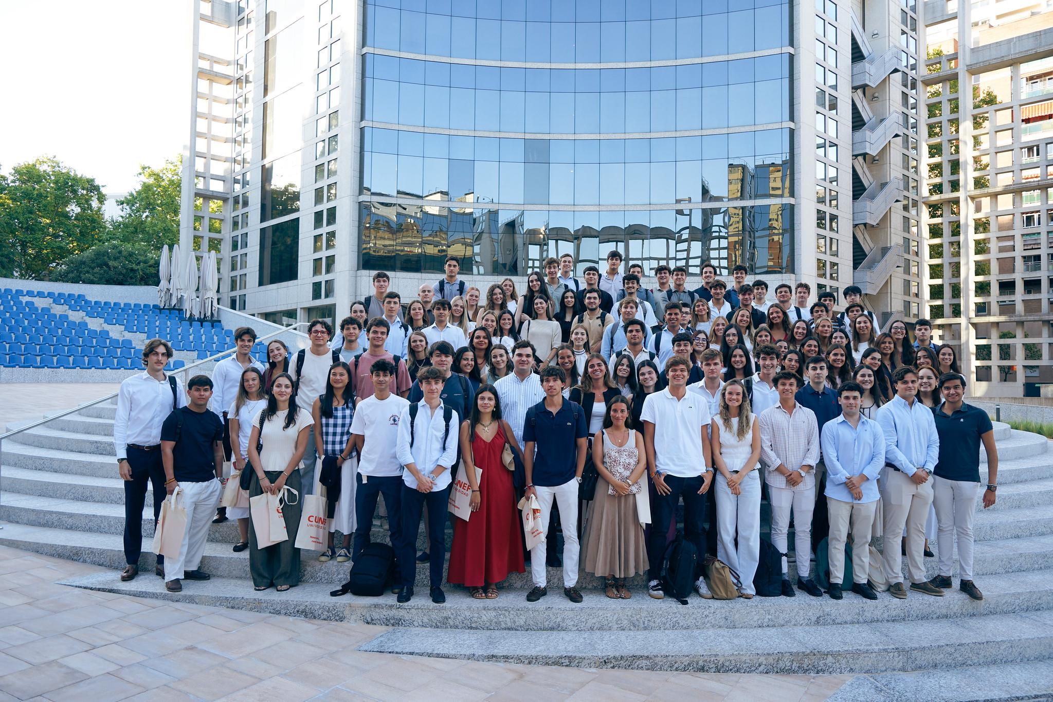 Un grupo grande de estudiantes posando frente a un edificio moderno y reflejante.