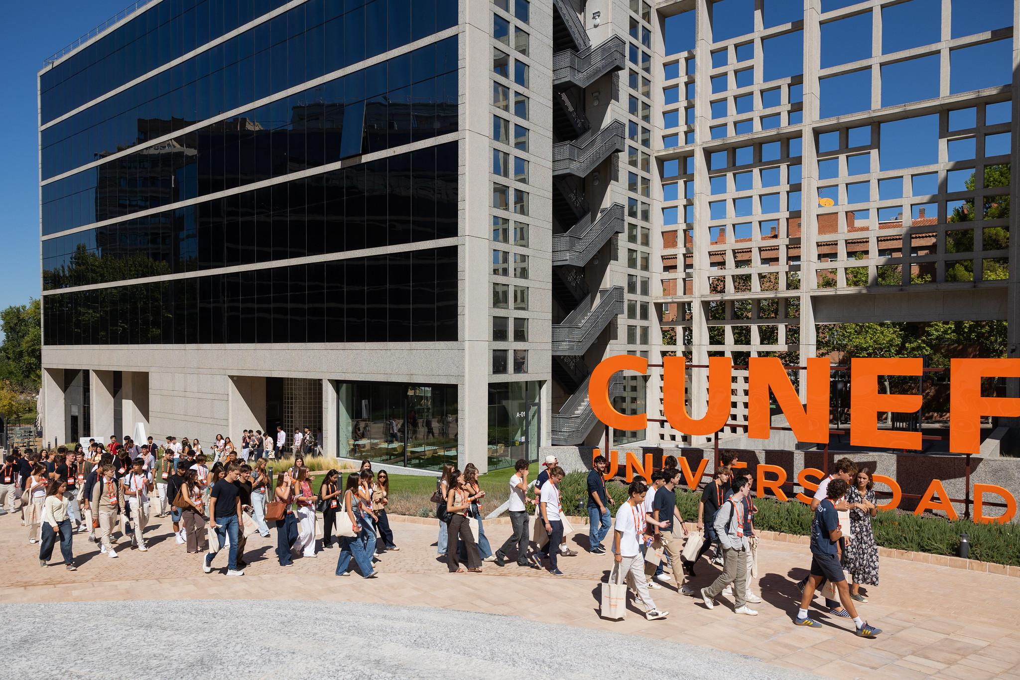 Un grupo de personas camina frente a un edificio moderno con letras grandes que dicen 'CUNEF Universidad'.