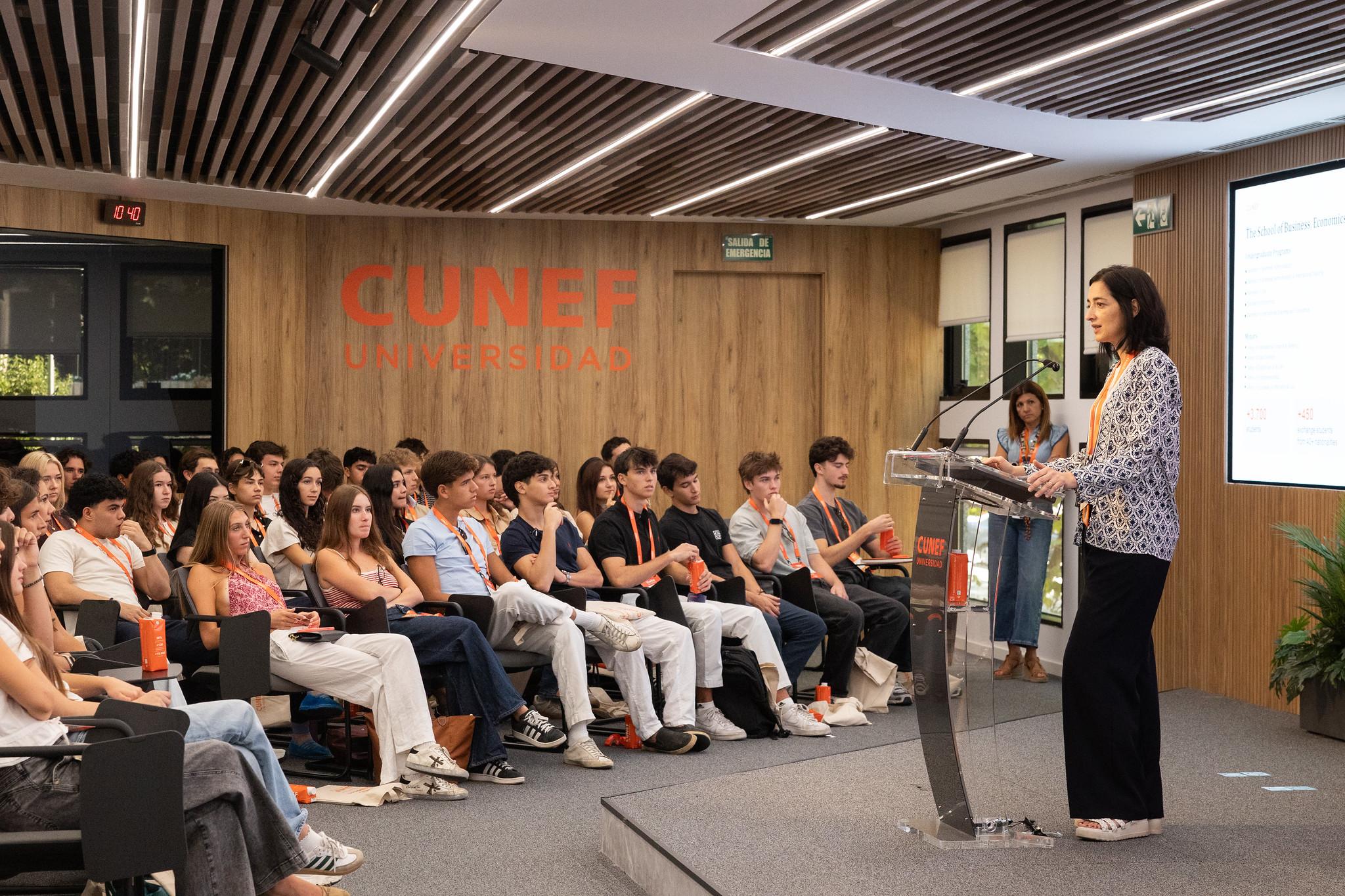 Una presentación en CUNEF con un grupo de estudiantes atendiendo a una ponente en el escenario.