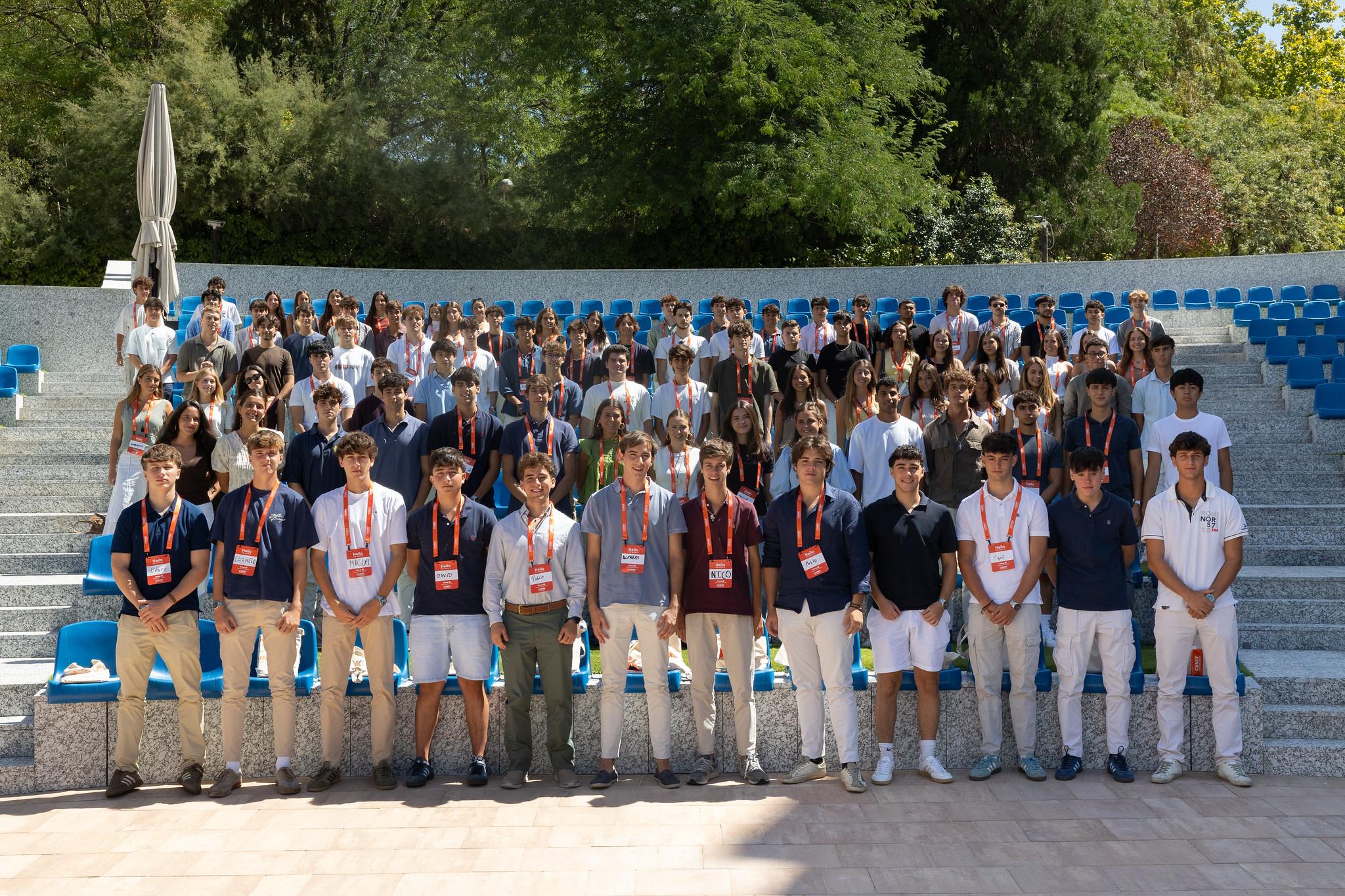 Un grupo grande de jóvenes posando en un lugar al aire libre, sobre gradas con sillas azules.