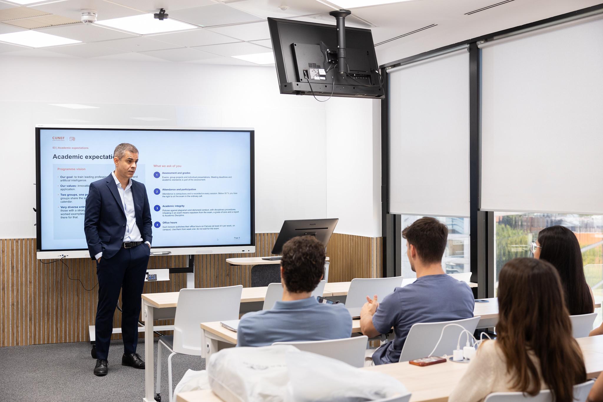 Un profesor está presentando en un aula moderna frente a un grupo de estudiantes atentos.